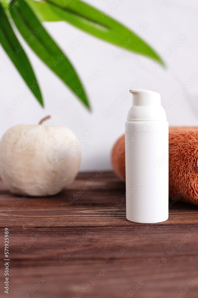White cosmetic bottle with towel on wooden table, bath staging White cosmetic bottle with towel on wooden table, bath staging