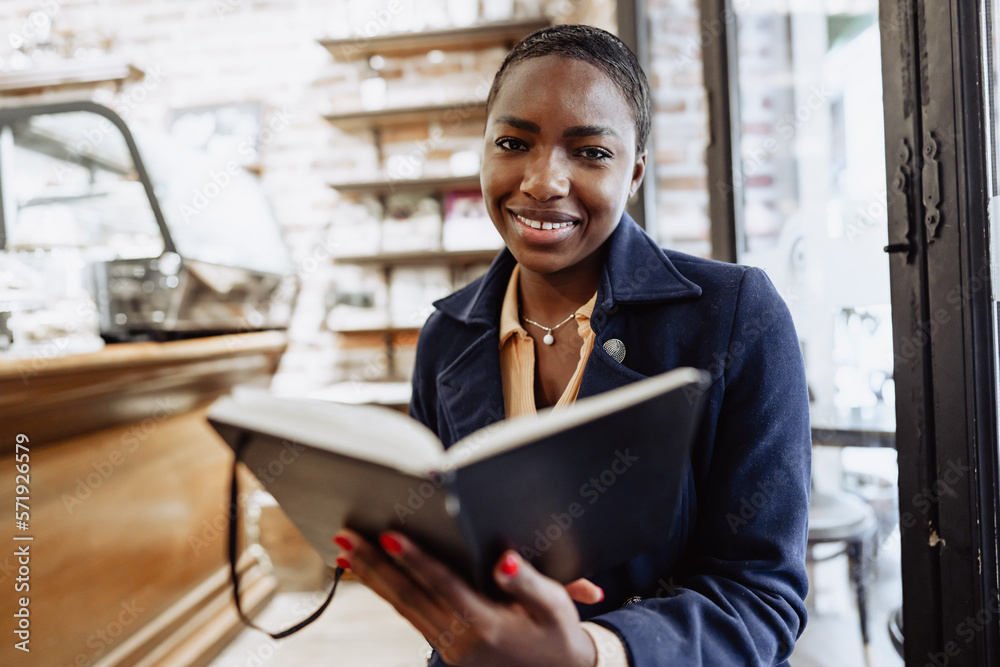 Fototapeta premium Beautiful african girl making notes in diary in cafeteria.