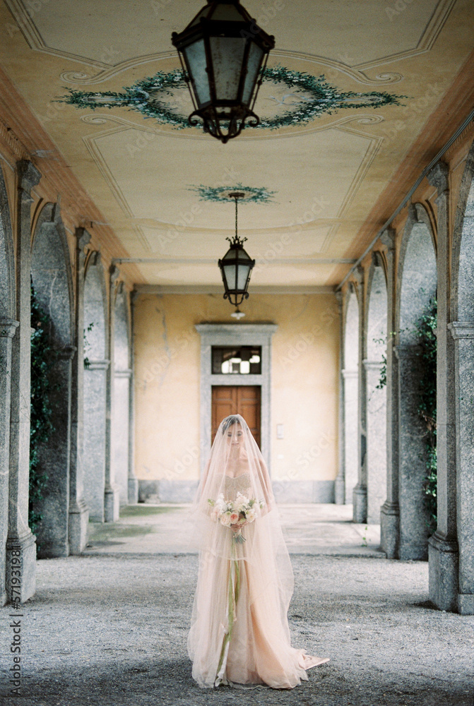 Bride in a dress with a veil walks with a bouquet along the terrace of an old villa
