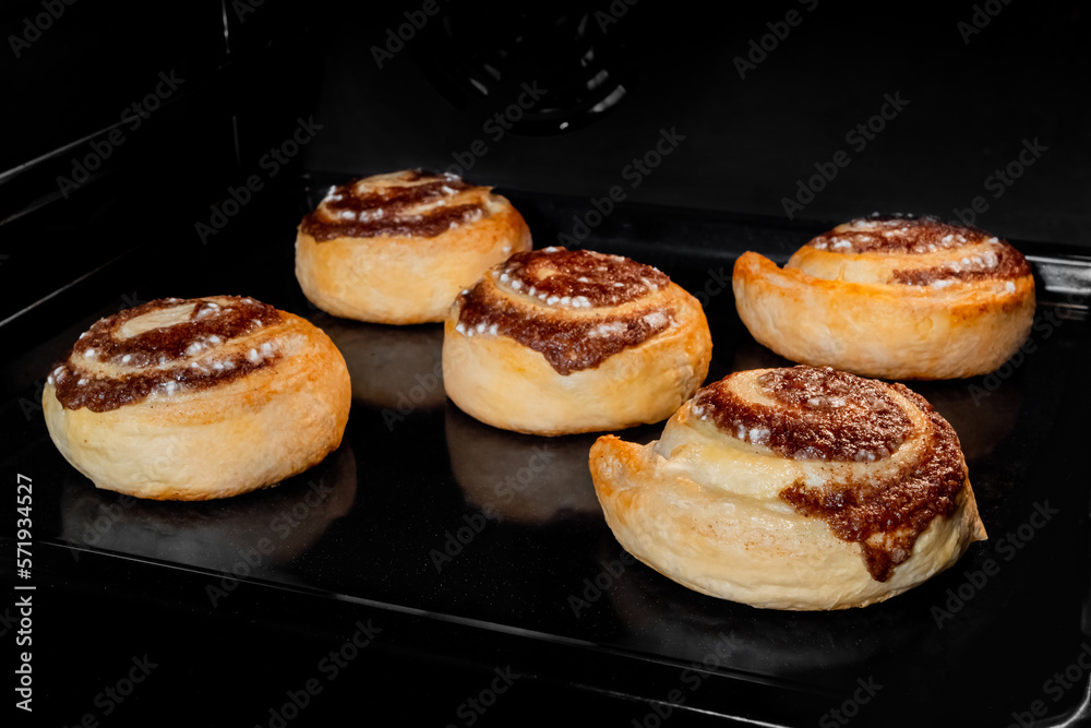 Five cinnamon buns baking and rising on tray in electric oven - close up view. Swedish cuisine, homemade bakery, food, cooking and pastry concept