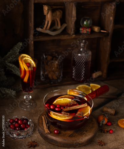 Mulled wine in glass saucepan with cinnamon sticks,anise,red wine,oranges with wooden box with christmas horse,glass ball with tree and fir branch.Christmas or New Year card.