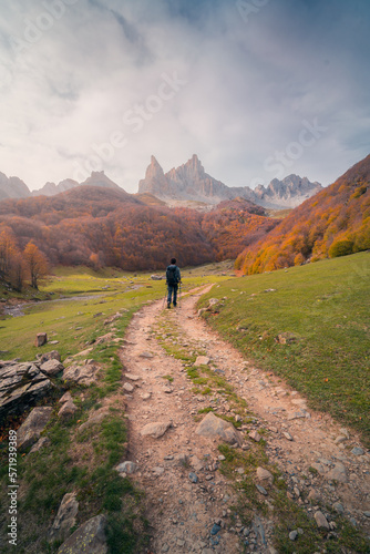 Hiker walking on pathway between autumn trees in mountains photo