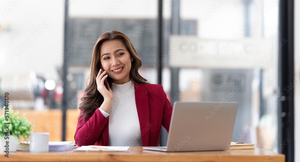 Smiling beautiful Asian businesswoman analyzing chart and graph showing changes on the market and holding smartphone at office Smiling beautiful Asian businesswoman analyzing chart and graph showing changes on the market and holding smartphone at office