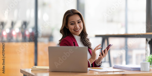 Happy businesswoman using mobile phone while working at office with laptop