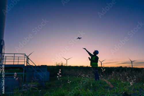 asian female engineer using drone for inspection wind turbine farm in evening.
