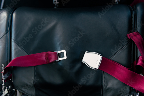 Red seat belt in airplane on black seat. Unlocked. Safety, prevention accident.