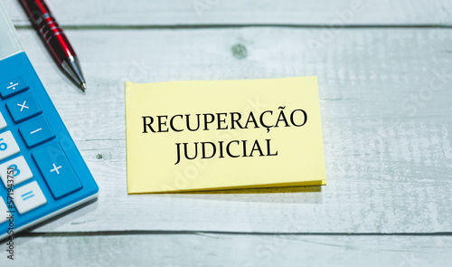 O texto Recuperação judicial em Português do Brasil escrito em um pedaço de papel que está sobre uma mesa de madeira. Uma calculadora e uma caneta na composição. Economia brasileira. photo
