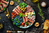 Italian snacks. Plate with cheese and ham, prosciutto, jamon salami, and snacks. On a black stone background.