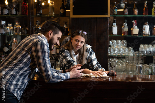 Young colleagues bartenders and waitress sit at the bar and get bored while the cafeteria is empty, spend time talking until the first guests arrive
