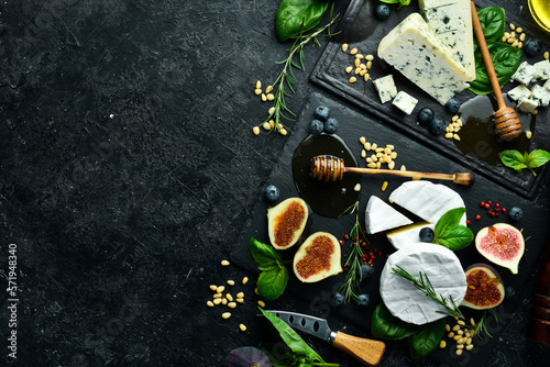 Assortment of cheese and snacks on stone black plates. Top view. On a black background.