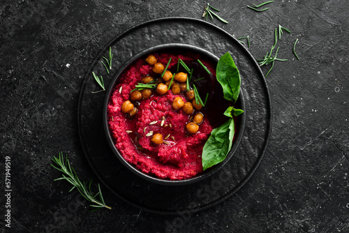 Beetroot chickpea hummus in a bowl. Red hummus. Healthy vegetarian food. On a concrete black background.