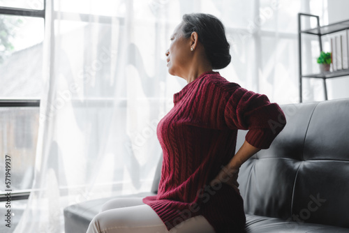 Free Download Elderly asian housewife woman sitting on sofa. Back pain, lumbar pain, cervical spine - GFXLoad