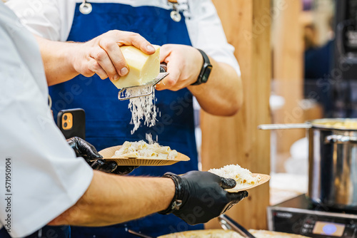 Quadro em tela Close up of male chef hands and an assistant grating cheese over pasta