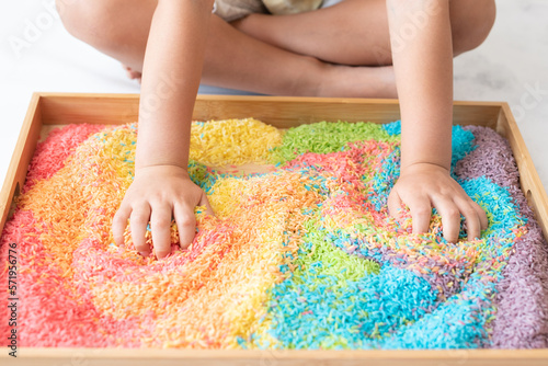 Two hands mixing colourful sensory bin