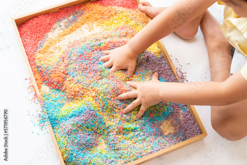 Two hands mixing colourful sensory bin photo