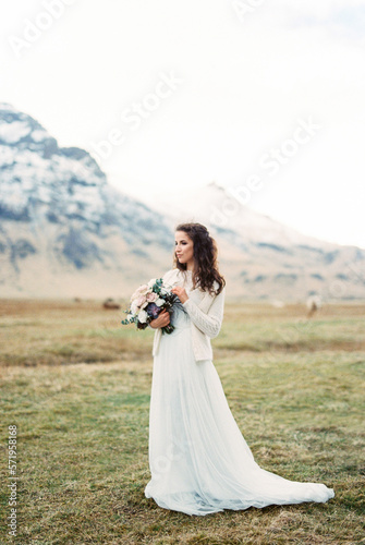 Bride with a bouquet stands on a lawn in a mountain valley. Iceland