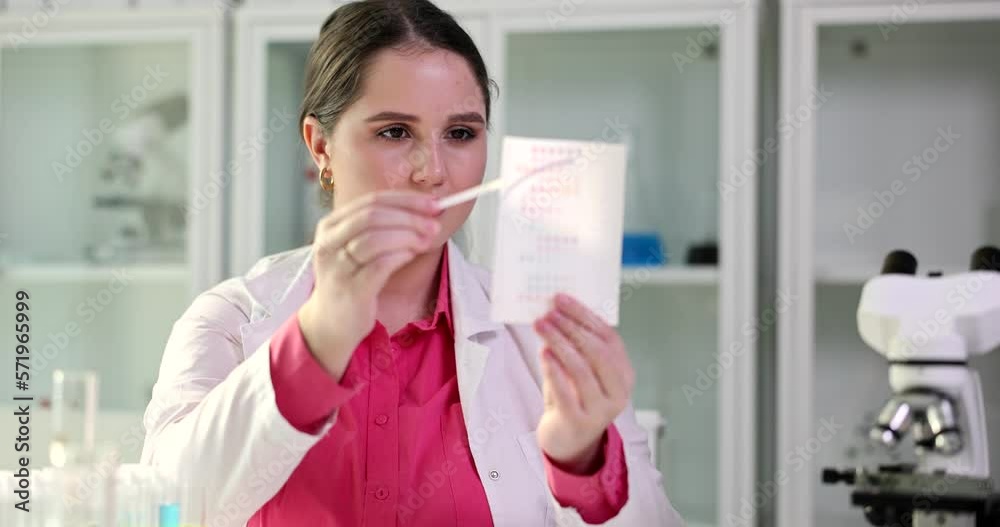 Female scientist looks at litmus strip and compares te results closeup Female scientist looks at litmus strip and compares te results closeup