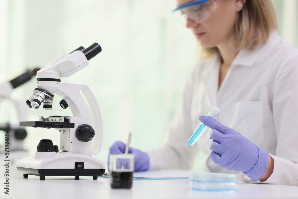 A woman in front microscope and blue reagent in test tube A woman in front microscope and blue reagent in test tube