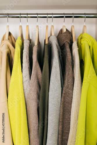 The basic wardrobe of a fashion stylist. Neutral colors: white, brown, beige, grey. Bright colors: yellow. White wardrobe, wooden hangers and towels
