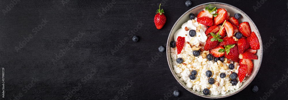 Cottage cheese, curd cheese with fresh strawberries, blueberries, nuts and yogurt in a bowl.  Healthy dairy product rich in calcium and protein. Top view, banner