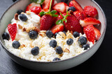 Cottage cheese, curd cheese with fresh strawberries, blueberries, nuts and yogurt in a bowl.  Healthy dairy product rich in calcium and protein.
