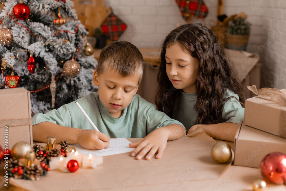 Naklejka premium boy and girl write a letter with Christmas wishes to Santa Claus, sitting at a wooden kitchen table