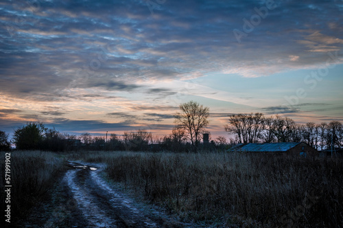 The field road between the villages is covered with puddles that reflect the colors of the dawn sun.