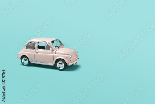 Miniature pale pink toy car on green background with copyspace