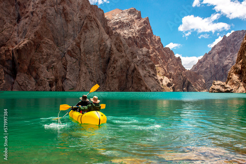 Kayaking on a mountain lake. Two men are sailing on a red canoe along the lake along the rocks. The theme of water sports and summer holidays. © Vera