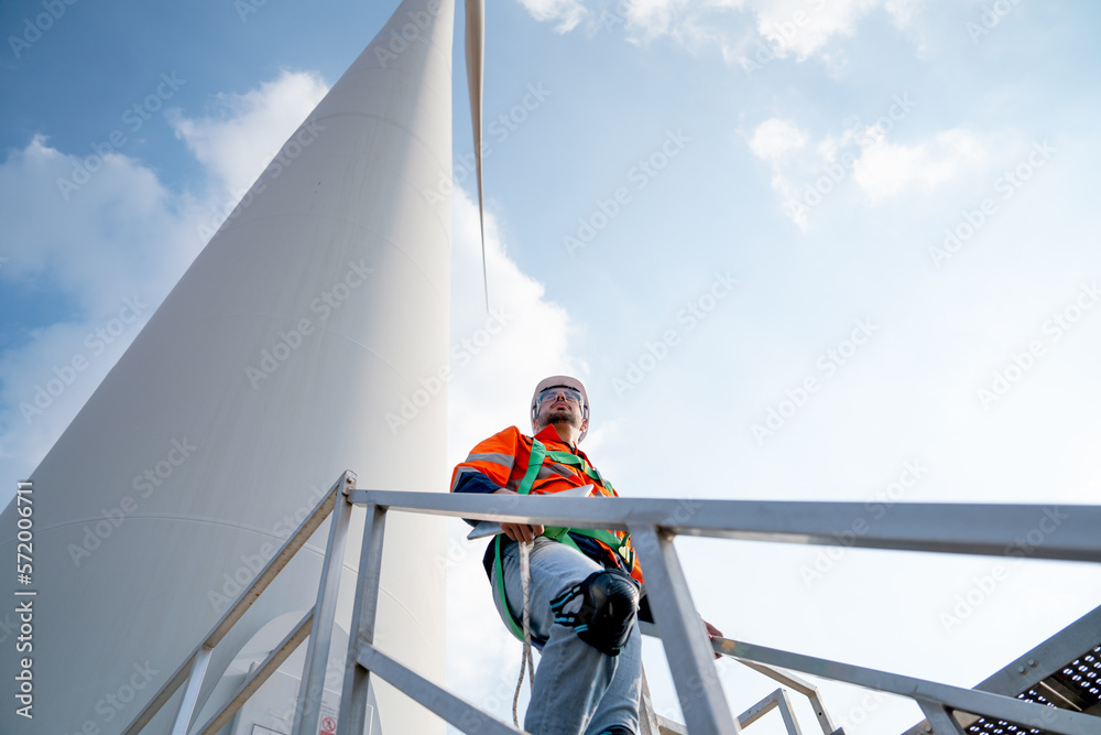 Caucasian engineer or technician walk down at base of windmill or wind turbine and look to right side and blue sky. Caucasian engineer or technician walk down at base of windmill or wind turbine and look to right side and blue sky.