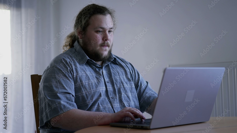 One casual overweight young man in front of laptop computer browsing internet at home One casual overweight young man in front of laptop computer browsing internet at home