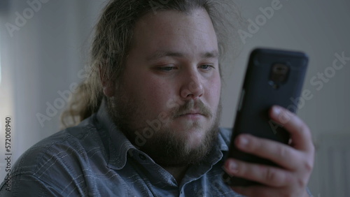 Close up young man looking at cellphone device. One overweight male person staring at phone