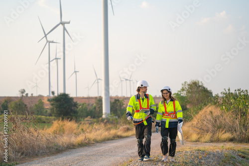 Two engineer or technician man and woman workers walk along the road far from windmill or wind turbine and talk together after finish work.