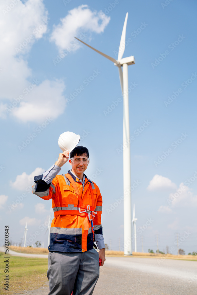 Engineer or technician worker stand in front of windmill or wind turbine and hold hardhat also look at camera in concept of confidence and happiness to work with green ecology support power. Engineer or technician worker stand in front of windmill or wind turbine and hold hardhat also look at camera in concept of confidence and happiness to work with green ecology support power.