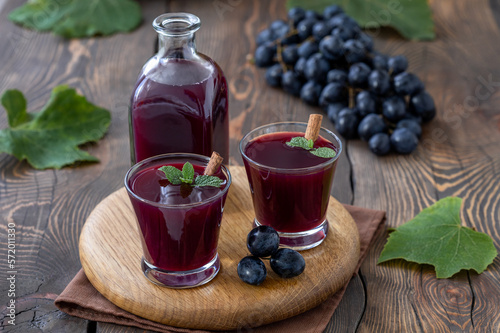 Homemade grape mors. A bottle and two glagges of fresh Black Grapes Juice with bunch of grapes on background. Dark wooden table, selective focus, horizontal.