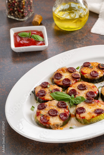 Mini zucchini pizza bites. Grilled zucchini slices with tomato sause, sausage, basil and melted mozzarella cheese served on a white plate. Selective focus, vertical.