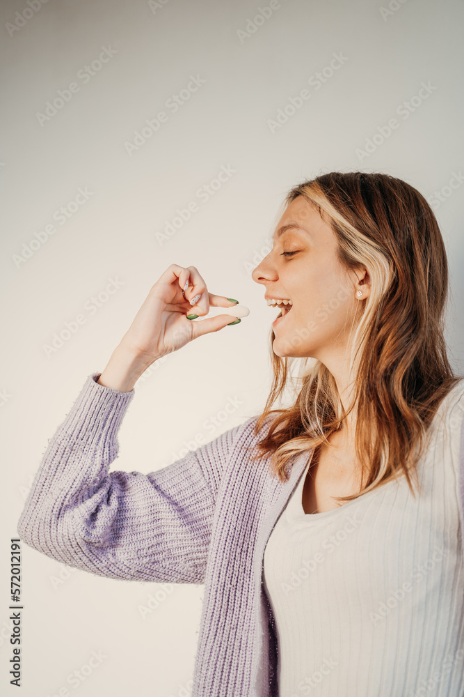 girl brings a pill to her mouth, her mouth is ajar, gray background girl brings a pill to her mouth, her mouth is ajar, gray background