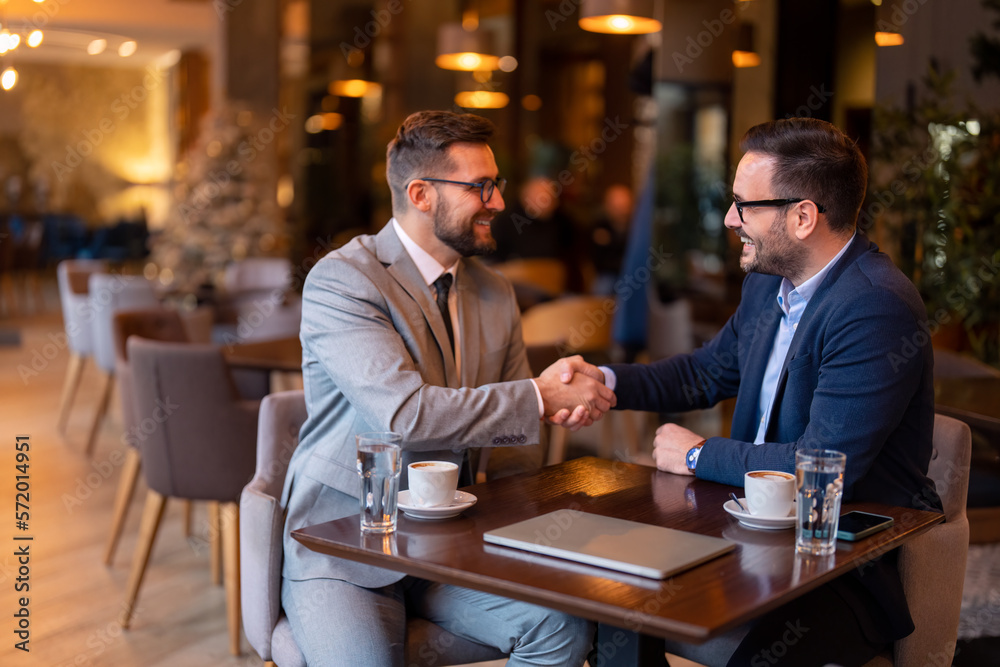 Two happy professional business men shaking hands after successful financial deal at business meeting in city restaurant. Businessman shaking hands with his partner celebrating successful teamwork.