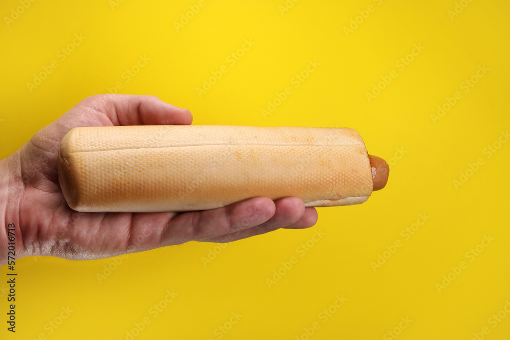 french hot dog with ketchup sauce in hand on yellow background french hot dog with ketchup sauce in hand on yellow background