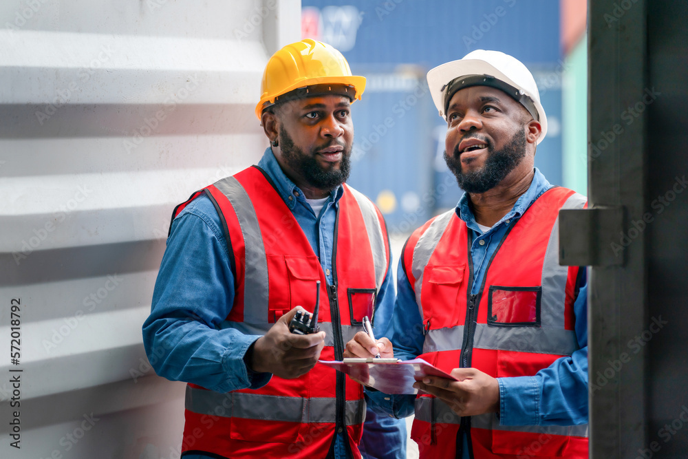 Portrait of Two African Engineer or foreman wears PPE checking container storage with cargo container background at sunset. Logistics global import or export shipping industrial concept. Portrait of Two African Engineer or foreman wears PPE checking container storage with cargo container background at sunset. Logistics global import or export shipping industrial concept.