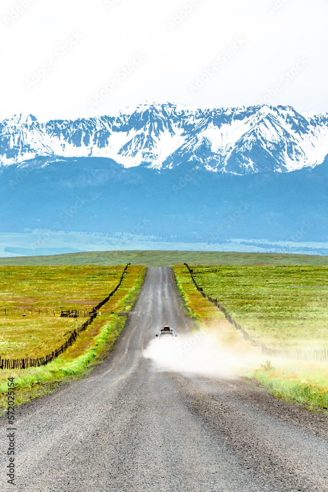 Naklejka premium Car Driving Down Dirt Road Towards Wallowa Mountain Range in Oregon