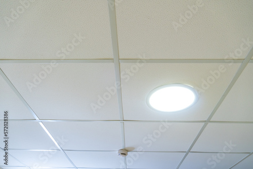 Suspended ceiling made of square plasterboard slabs with built-in round LED lighting. Close-up details of the ceiling in the office and an autonomous fire detector.