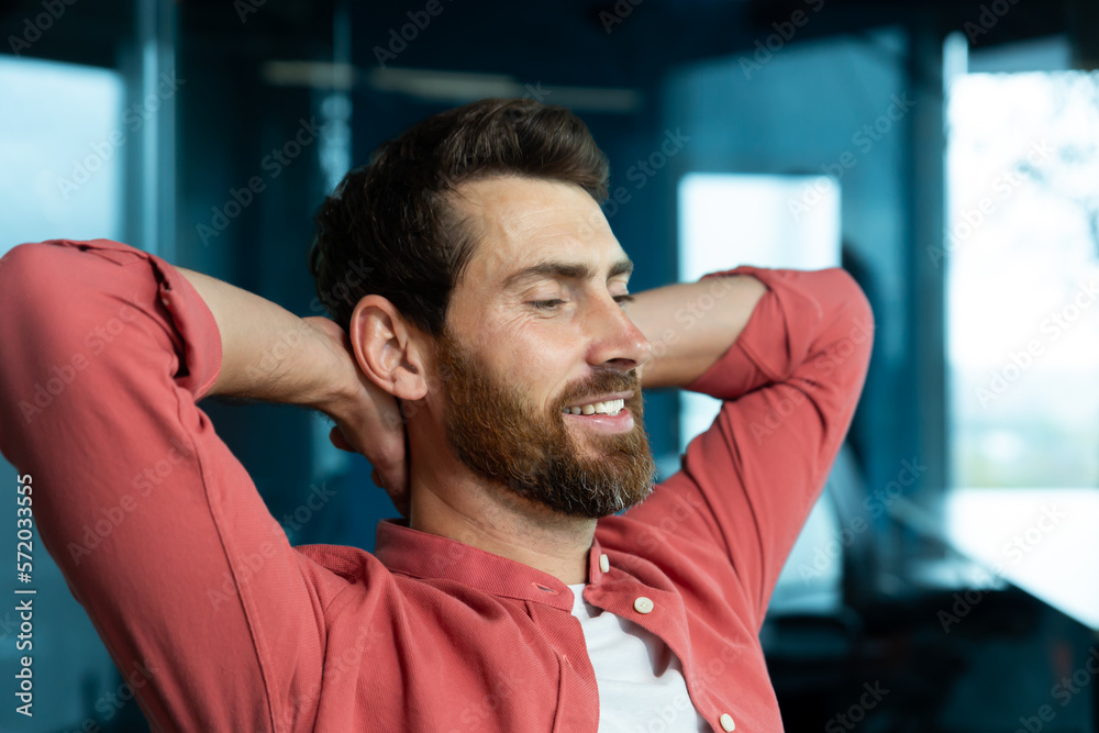 A young male programmer, a freelancer, is resting from a hard day in the office at his desk. He sits on a chair, closes his eyes, puts his hands behind his head, meditates, dreams, smiles. A young male programmer, a freelancer, is resting from a hard day in the office at his desk. He sits on a chair, closes his eyes, puts his hands behind his head, meditates, dreams, smiles.