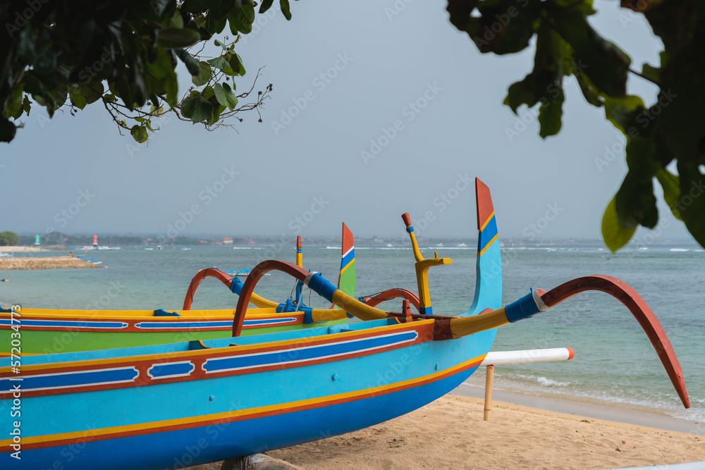 Colorful traditional longtail boat under beach tree, close up view, dark rainy sky at background, Sanur beach, Bali, Indonesia
