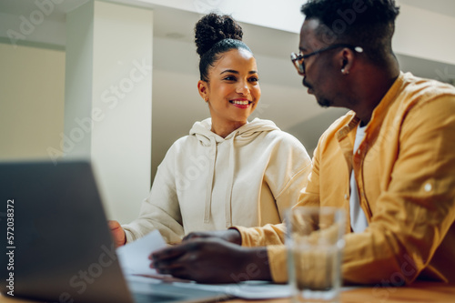 Diverse couple using laptop while sitting at the table at home