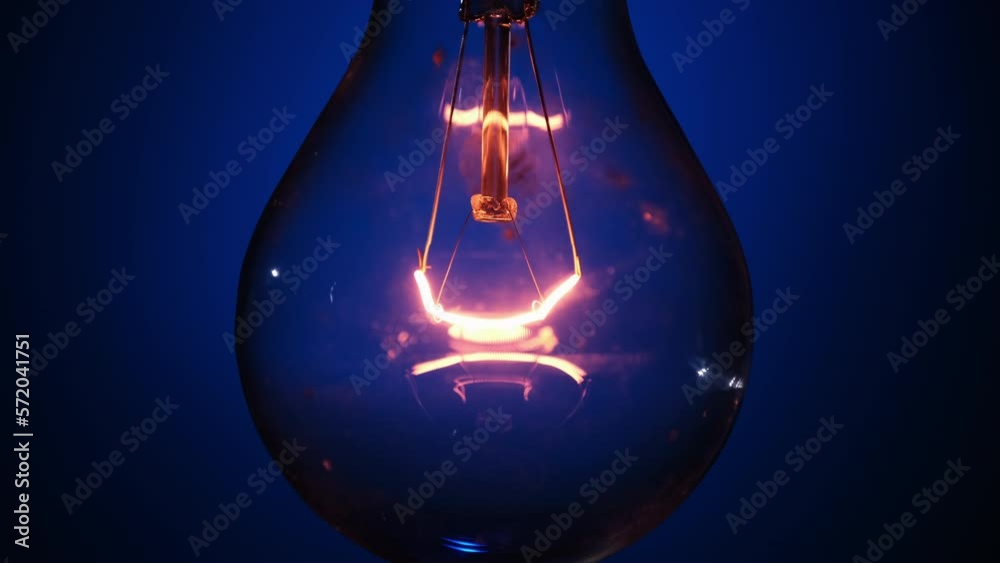 Incandescent bulb glows and flickers on dark blue background. Edison