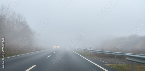 Auto fährt im Nebel auf einer Straße. Die Scheinwerfer leuchten hell. 