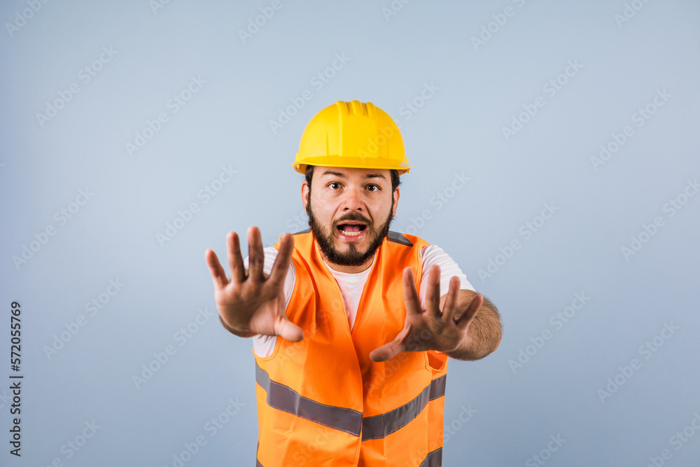 portrait of Hispanic bearded young man engineering and worker with hard helmet in Mexico Latin America on blue background	