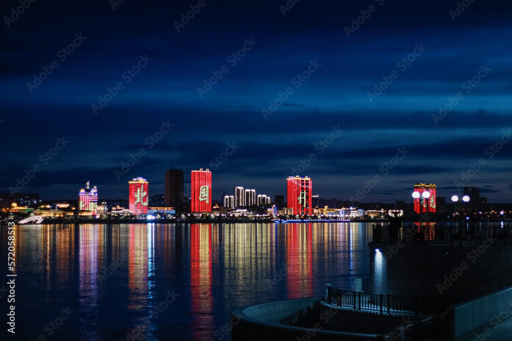 View of the Chinese city at night. Neon illumination of houses on the Amur River.