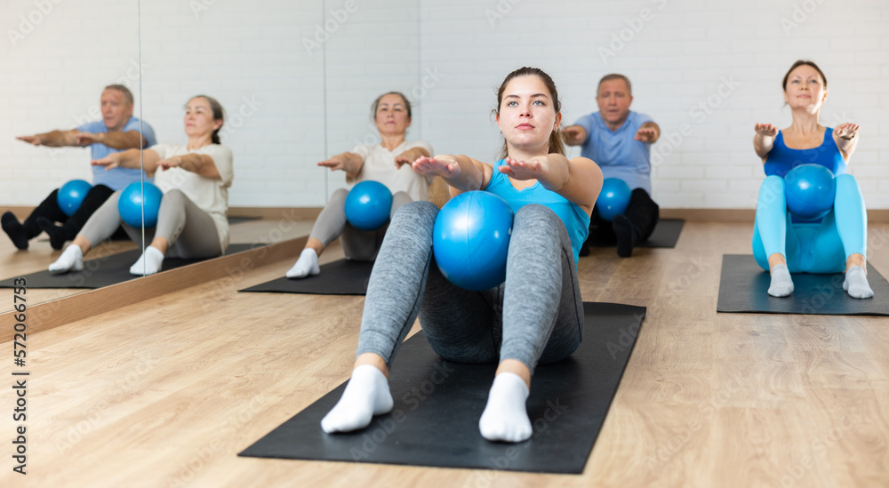 Fototapeta premium Slim young woman engaging in pilates training with ball in gym room during workout session. Persons practicing pilates in fitness studio